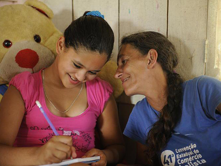 Foto do Projeto Resgate - Uma criança escreve num caderno enquanto um adulto sorri para ela